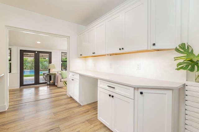 kitchen featuring white cabinets, built in desk, light wood-type flooring, and french doors