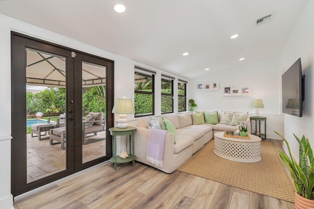 living room with french doors, vaulted ceiling, and light wood-type flooring