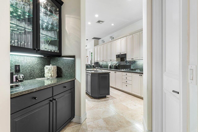 kitchen with backsplash, dark stone countertops, white cabinetry, and cream cabinets