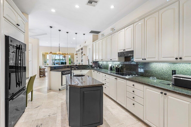 kitchen featuring kitchen peninsula, decorative backsplash, black refrigerator, dark stone counters, and decorative light fixtures