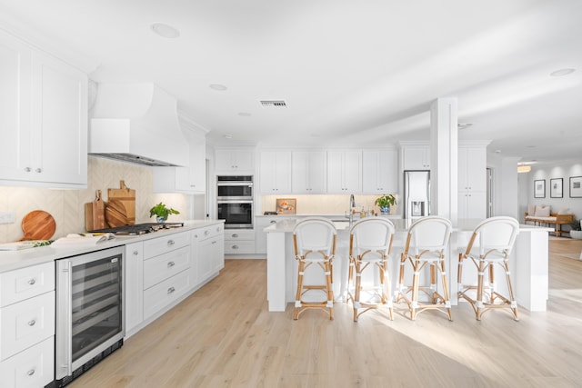 kitchen featuring a breakfast bar, white cabinetry, a kitchen island with sink, stainless steel appliances, and beverage cooler