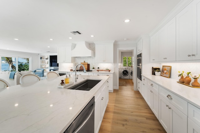 kitchen with custom exhaust hood, stainless steel appliances, washer and dryer, white cabinets, and sink