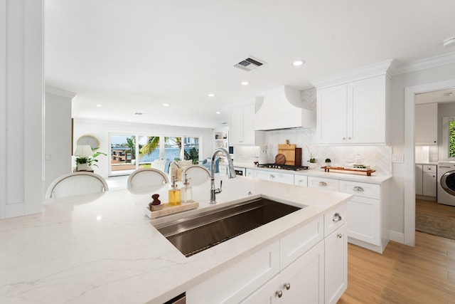 kitchen with premium range hood, sink, white cabinetry, light stone countertops, and separate washer and dryer