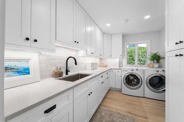 laundry area with light hardwood / wood-style flooring, washing machine and dryer, sink, and cabinets