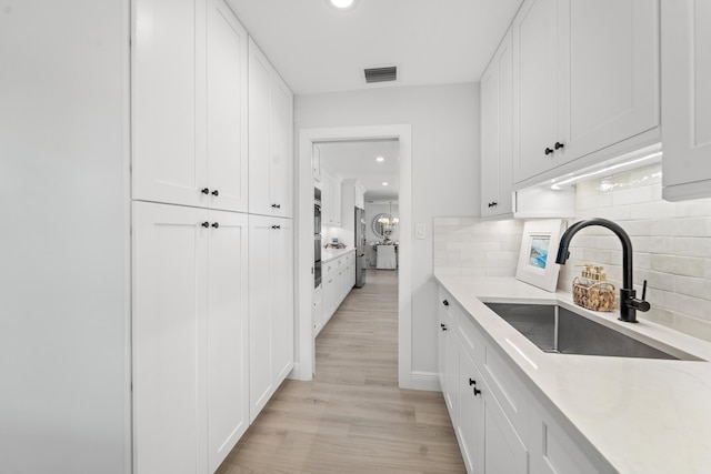 kitchen with decorative backsplash, sink, white cabinetry, and light hardwood / wood-style floors