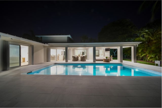 pool at night with a patio area and outdoor lounge area