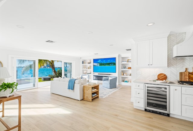 living room featuring beverage cooler, ornamental molding, bar, and light wood-type flooring