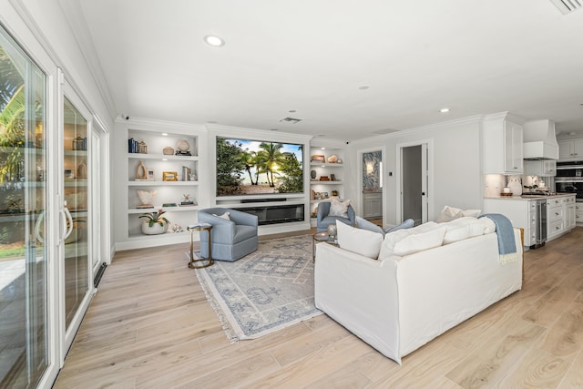 living room with built in shelves, light hardwood / wood-style flooring, and crown molding