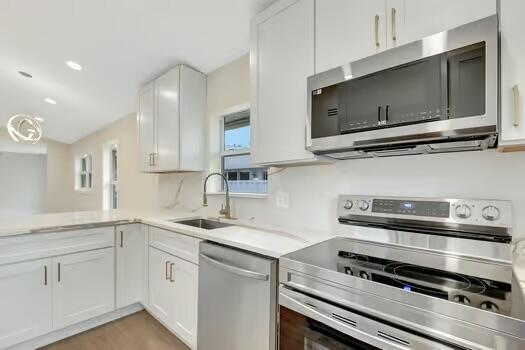 kitchen with appliances with stainless steel finishes, light wood-type flooring, white cabinetry, and sink