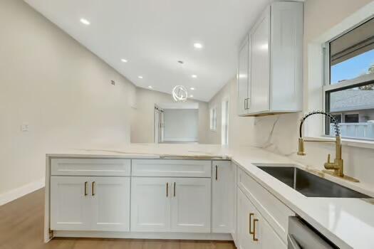 kitchen featuring lofted ceiling, sink, stainless steel dishwasher, light wood-type flooring, and white cabinetry