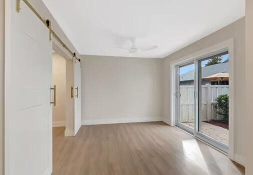 unfurnished room with ceiling fan, a barn door, and light wood-type flooring