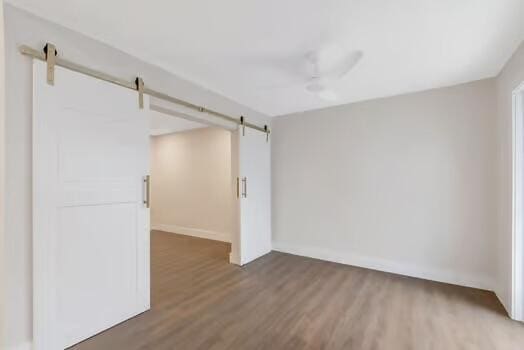 unfurnished room featuring a barn door, ceiling fan, and dark wood-type flooring