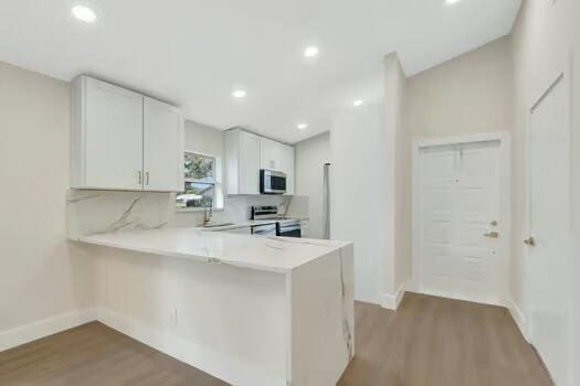 kitchen featuring kitchen peninsula, hardwood / wood-style floors, stainless steel appliances, and white cabinetry