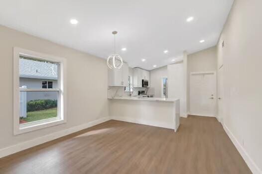 kitchen with kitchen peninsula, white cabinetry, hardwood / wood-style floors, and decorative light fixtures