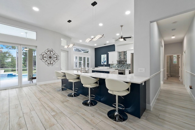 kitchen with ceiling fan, kitchen peninsula, pendant lighting, a breakfast bar area, and white cabinets