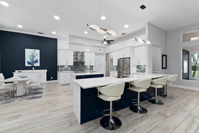 kitchen featuring wall chimney exhaust hood, white cabinets, decorative light fixtures, and light wood-type flooring