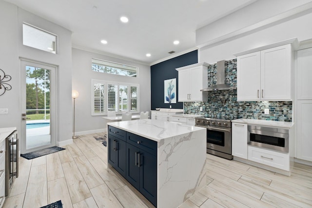 kitchen featuring light stone countertops, ornamental molding, wall chimney exhaust hood, stainless steel appliances, and white cabinets