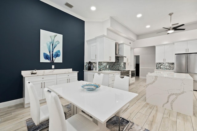 kitchen with stainless steel appliances, wall chimney range hood, a kitchen island, light hardwood / wood-style flooring, and white cabinets