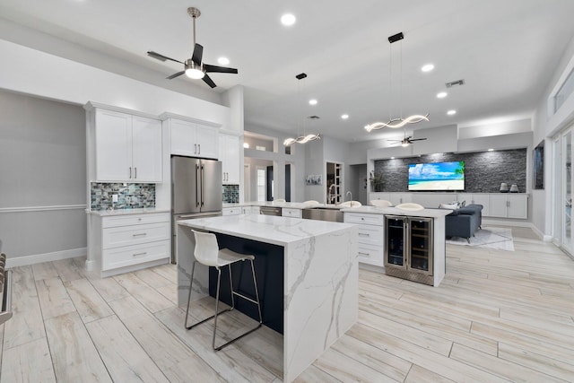 kitchen with beverage cooler, a spacious island, decorative backsplash, high end fridge, and white cabinets