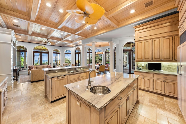 kitchen with ornate columns, a center island with sink, light stone counters, and wood ceiling