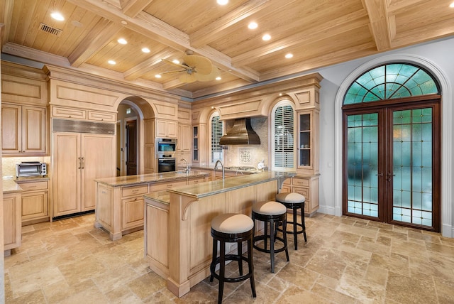 kitchen featuring wooden ceiling, an island with sink, wall chimney exhaust hood, and paneled built in refrigerator