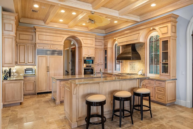 kitchen featuring light brown cabinetry, an island with sink, a kitchen breakfast bar, stainless steel appliances, and custom range hood