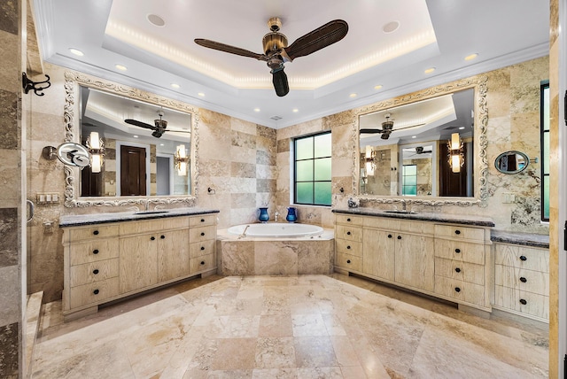 bathroom with tile walls, ornamental molding, vanity, a raised ceiling, and tiled bath