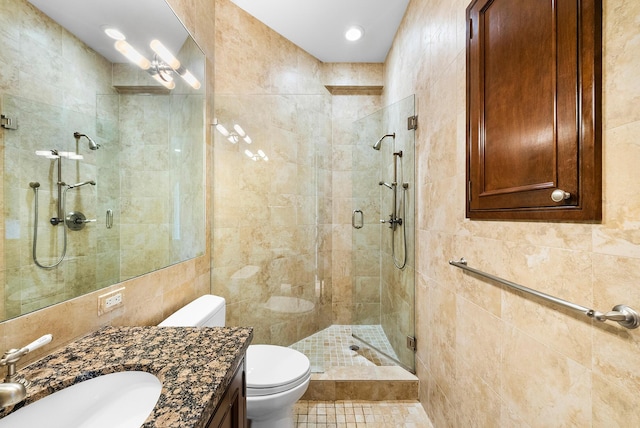 bathroom with a shower with door, vanity, tile walls, and toilet