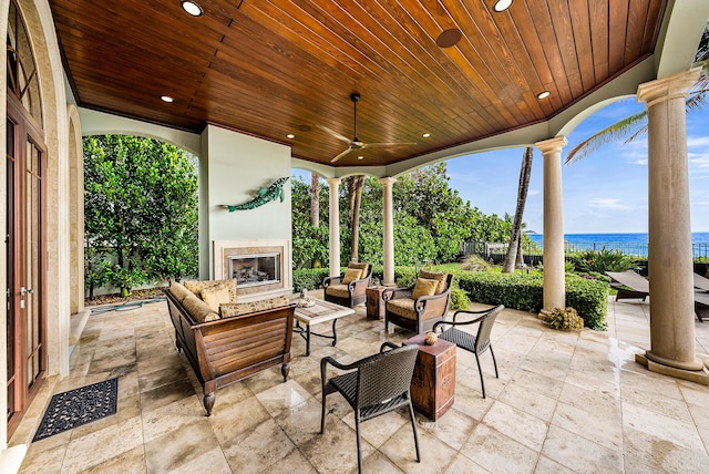 view of patio featuring a water view, an outdoor living space with a fireplace, and ceiling fan