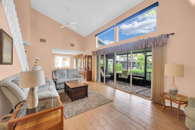 living room with ceiling fan with notable chandelier, light hardwood / wood-style floors, and high vaulted ceiling