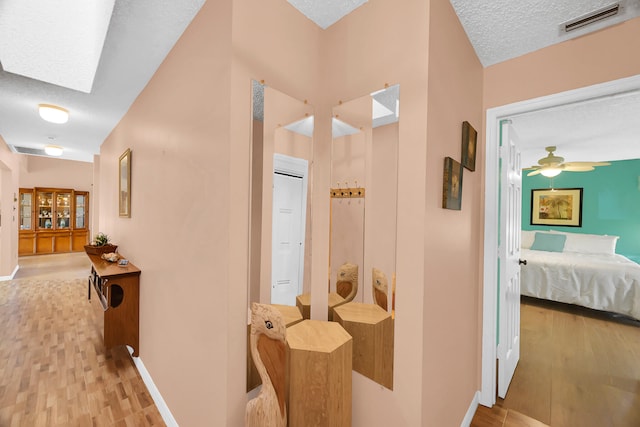 corridor featuring a skylight, light hardwood / wood-style floors, and a textured ceiling