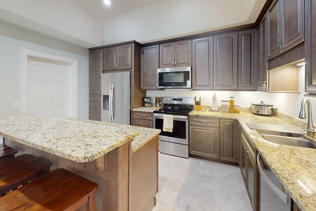 kitchen with a breakfast bar area, light stone counters, sink, and stainless steel appliances