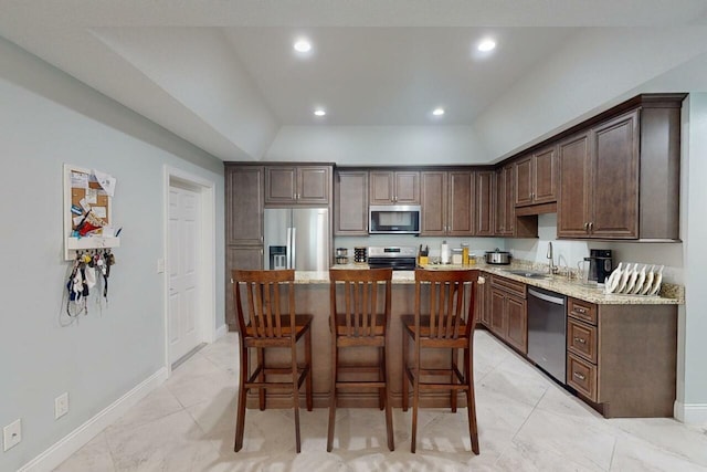 kitchen with dark brown cabinetry, light stone countertops, a kitchen island, and appliances with stainless steel finishes