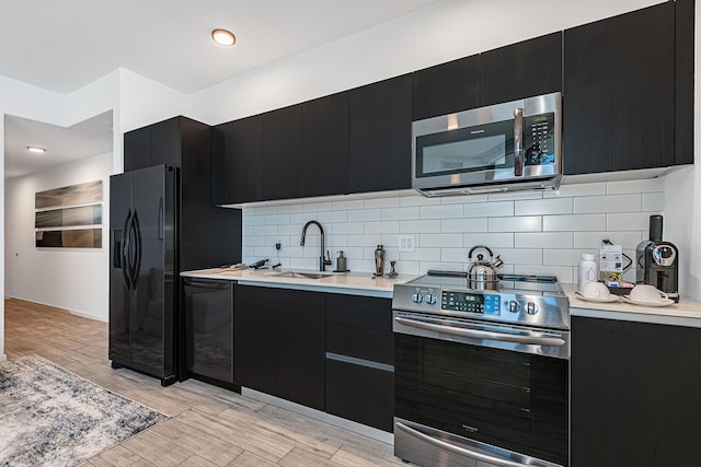 kitchen featuring black appliances, backsplash, light wood-type flooring, and sink