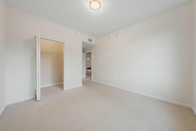 unfurnished bedroom featuring a walk in closet, light carpet, and a closet