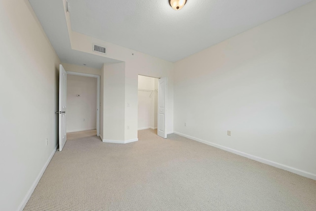 unfurnished bedroom with light colored carpet, a spacious closet, and a closet