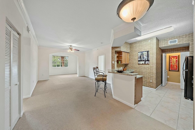 kitchen featuring black refrigerator, crown molding, ceiling fan, light colored carpet, and brick wall