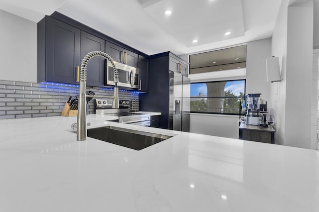 kitchen with tasteful backsplash, a raised ceiling, light stone countertops, and appliances with stainless steel finishes