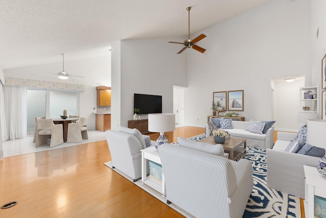 living room with ceiling fan, high vaulted ceiling, a textured ceiling, and light wood-type flooring