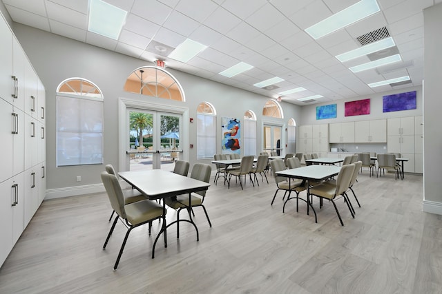 dining space featuring light wood finished floors, visible vents, a drop ceiling, a towering ceiling, and french doors