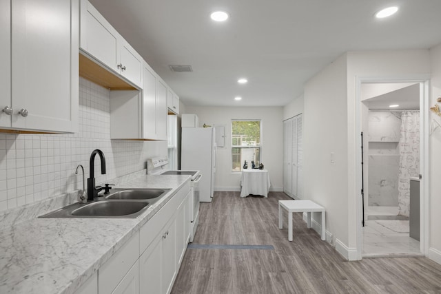 kitchen with white appliances, backsplash, sink, light hardwood / wood-style floors, and white cabinetry