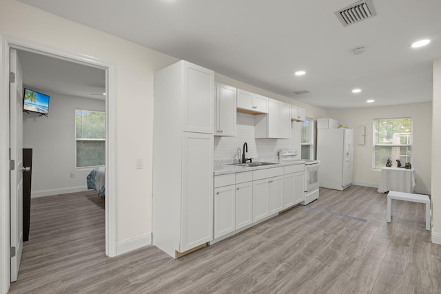 kitchen with white cabinetry, a wealth of natural light, white appliances, and light wood-type flooring