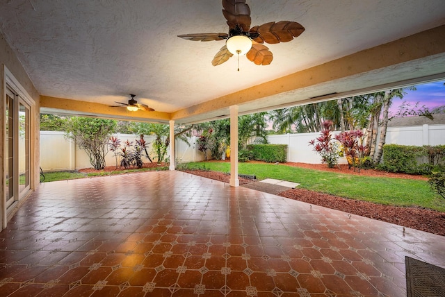 patio terrace at dusk featuring ceiling fan and a yard