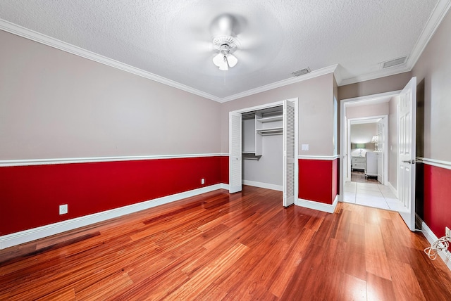 unfurnished bedroom featuring ceiling fan, wood-type flooring, a textured ceiling, and ornamental molding