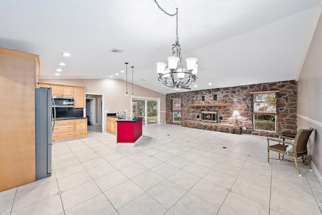 kitchen with a center island, a stone fireplace, a notable chandelier, light tile patterned floors, and appliances with stainless steel finishes