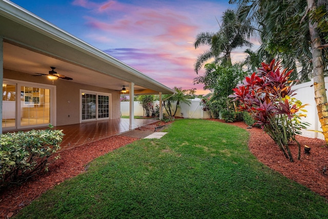 yard at dusk with ceiling fan and a patio area