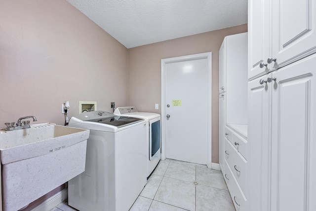 clothes washing area with cabinets, a textured ceiling, washing machine and clothes dryer, and sink