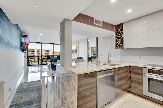 kitchen with sink, kitchen peninsula, light stone counters, white cabinetry, and stainless steel appliances