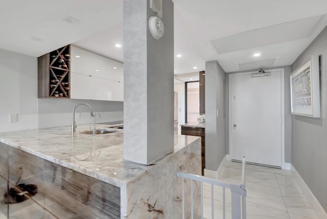 kitchen featuring white cabinets, kitchen peninsula, light stone countertops, and sink