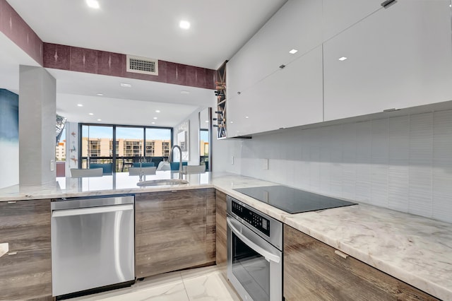 kitchen featuring sink, kitchen peninsula, decorative backsplash, appliances with stainless steel finishes, and white cabinetry